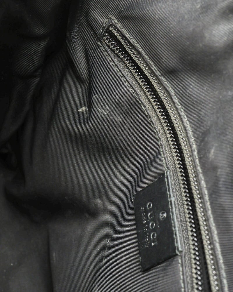 Vintage Gucci Messenger Bag interior detail with zipped pocket, leather brand tab, and marks on the black lining.