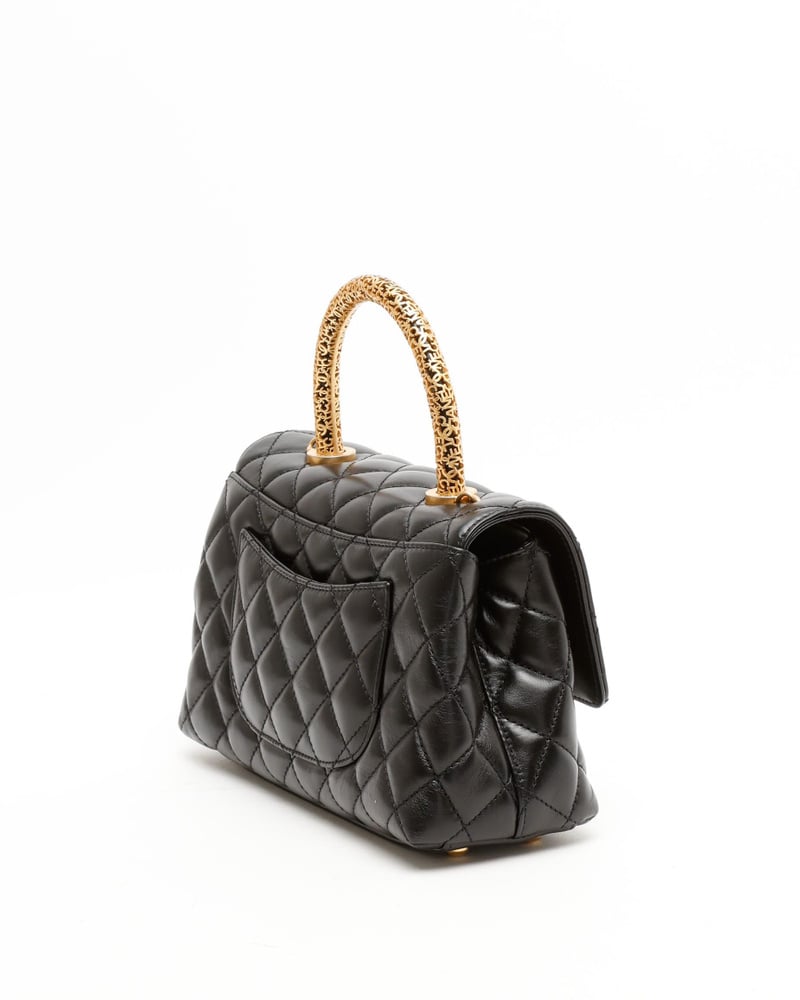 Schräge Rückansicht der Chanel Small Coco Handle Tasche aus schwarzem Steppleder mit verziertem, goldenem Griff.