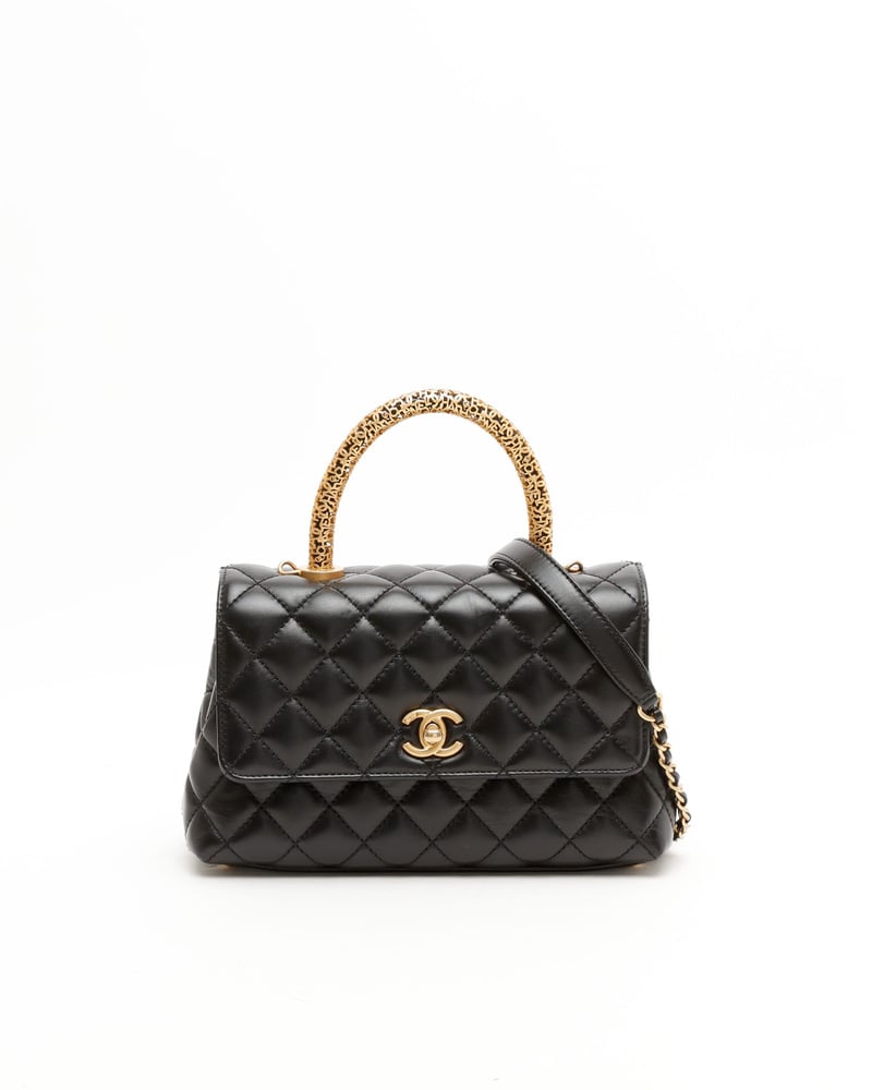 Vorderansicht einer kleinen Chanel Coco Handle Tasche aus schwarzem Steppleder mit kunstvoll verzierten, goldfarbenen Griff.