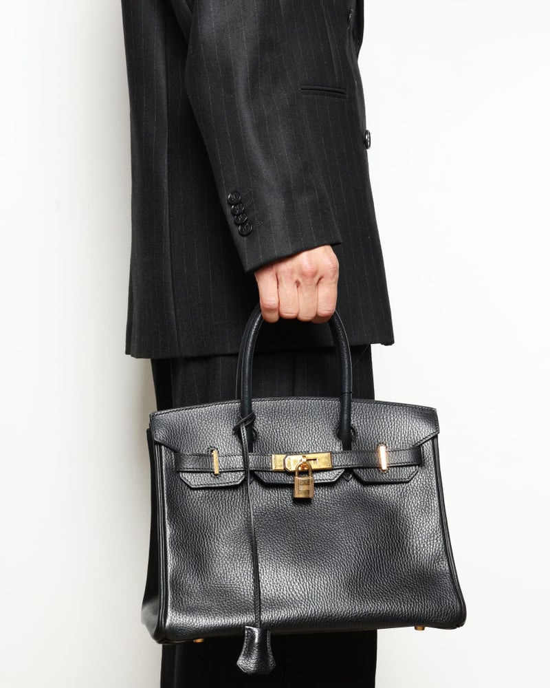 Ein Model in einem dunklen Nadelstreifenanzug trägt die Hermès Birkin 30 Epsom Tasche zur Größenveranschaulichung.