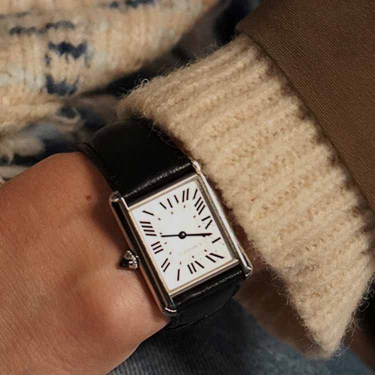 A gold and silver wristwatch and several delicate gold necklaces displayed on a soft, textured pink fabric background.