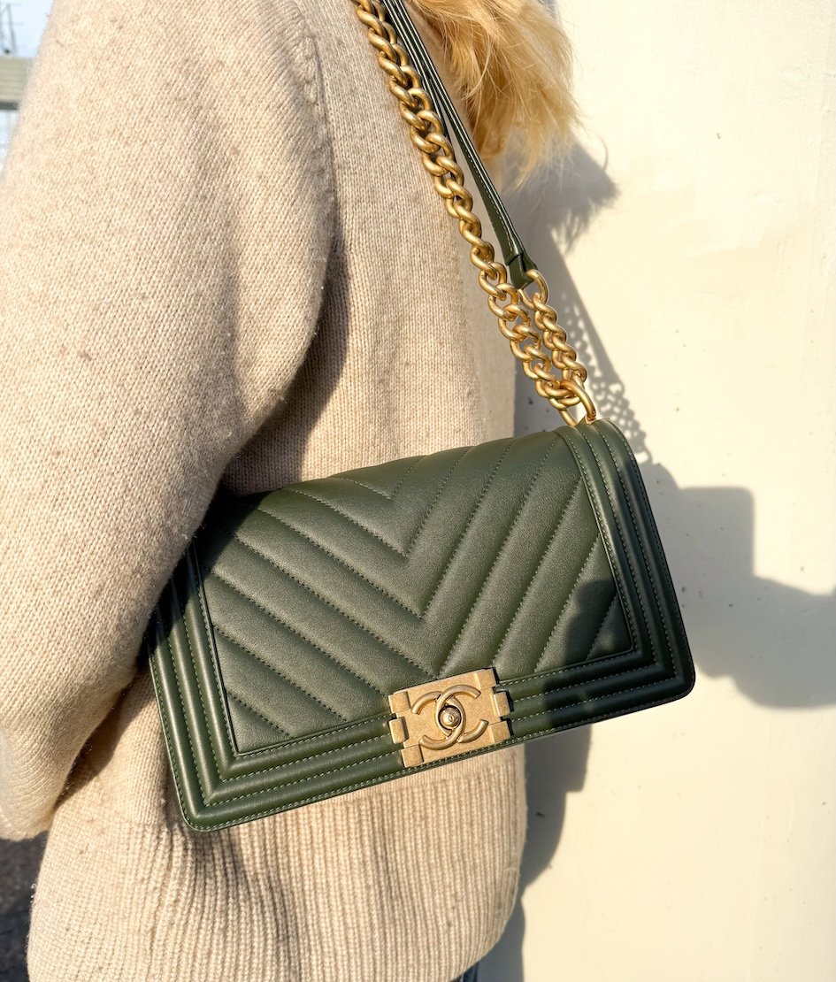 Dark green Chanel bag with gold chain strap on a person in a beige sweater.