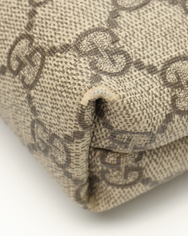 A close-up view of the Gucci Messenger Bag's corner, showing scuffing on the beige GG Supreme canvas.