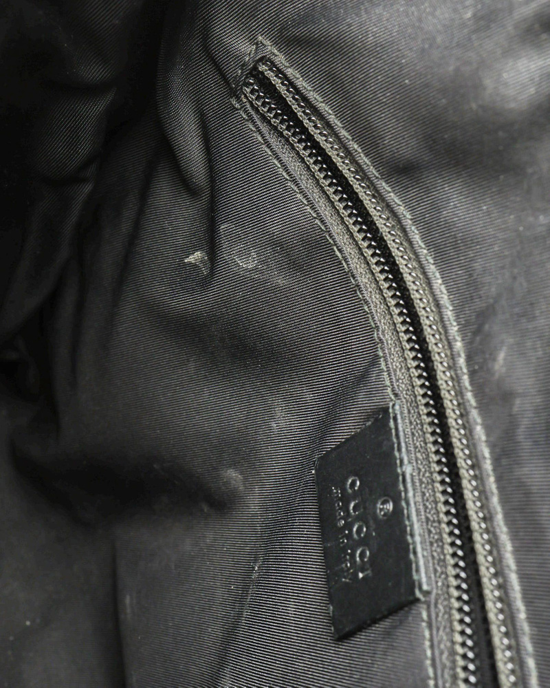 Vintage Gucci Messenger Bag interior detail with zipped pocket, leather brand tab, and marks on the black lining.