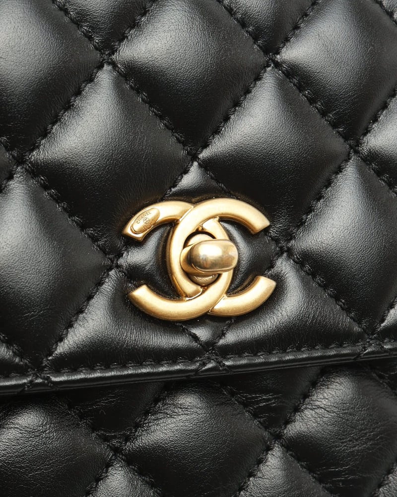 Nahaufnahme des goldfarbenen CC-Verschlusses auf dem schwarzen Rautensteppleder der Chanel Small Coco Handle Tasche.