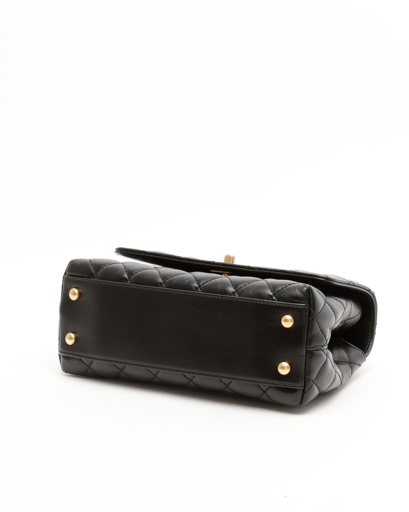 Bodenansicht einer schwarzen Chanel Small Coco Handle Tasche aus gestepptem Leder, mit vier goldfarbenen Schutzfüßen.