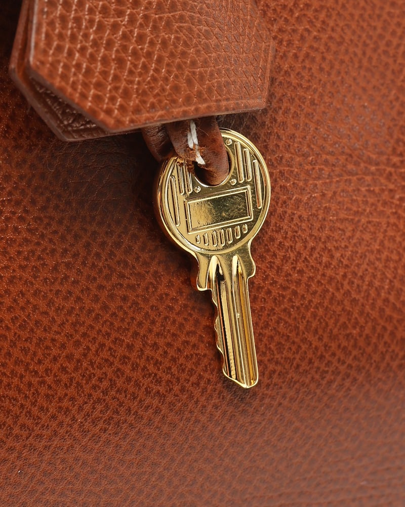 Nahaufnahme des goldfarbenen Schlüssels der Hermès Birkin 30 Tasche auf dem braunen Epsom-Leder.