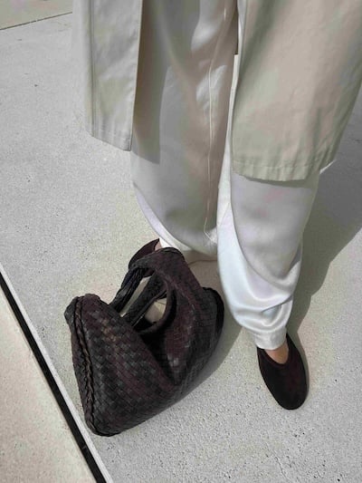 Person in light clothing with a dark woven bag on the ground by their feet.