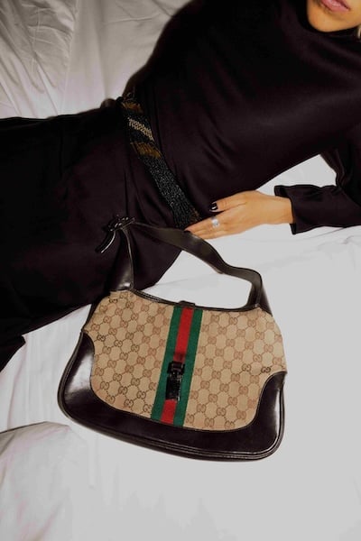 Person in a black dress holding a brown Gucci bag with red and green strap.