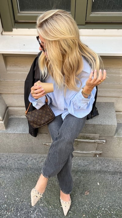 Person with Louis Vuitton shoulder bag sits on bench holding coffee.