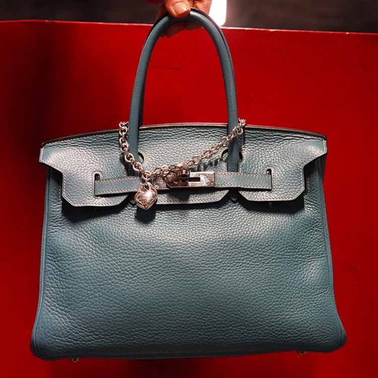 Woman in light jacket and sunglasses holding a brown Louis Vuitton bag with a patterned scarf.